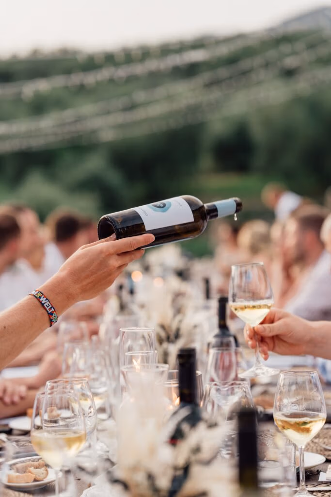 Hands pouring a bottle of white wine into a glass at an outdoor dinner party