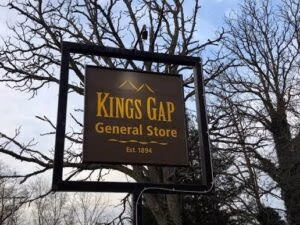 Sign for Kings Gap General Store with 'Est. 1894' hanging between bare trees outdoors